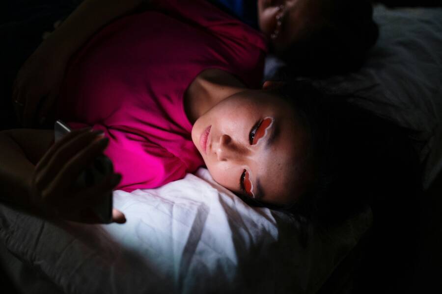 Asian woman lying in bed using smartphone in dark room, illustrating digital distraction