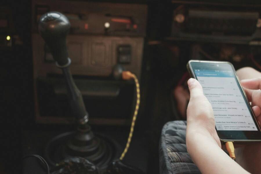 Person using smartphone in vintage car interior, connected through cable