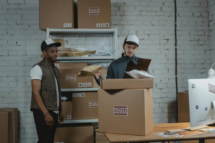 Two workers in a warehouse handling and checking fragile labeled packages before shipping