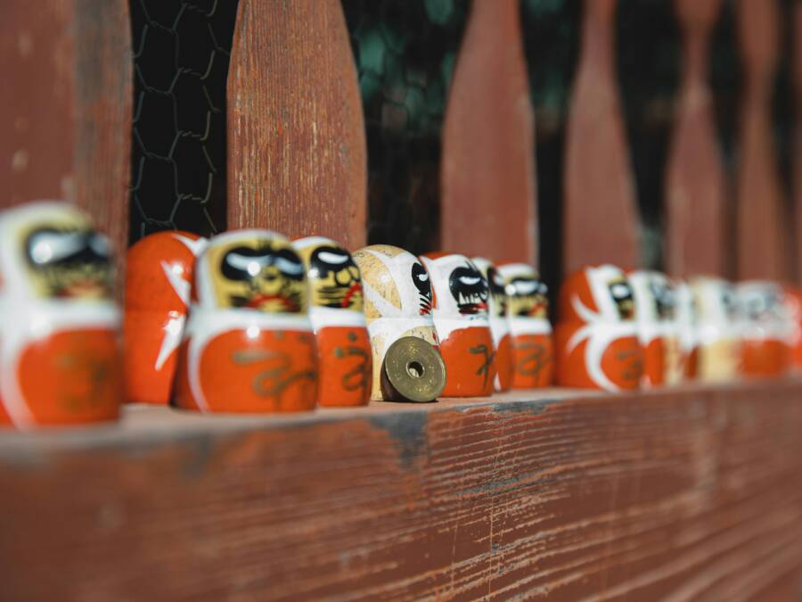 Colorful daruma dolls line up on a rustic wooden fence
