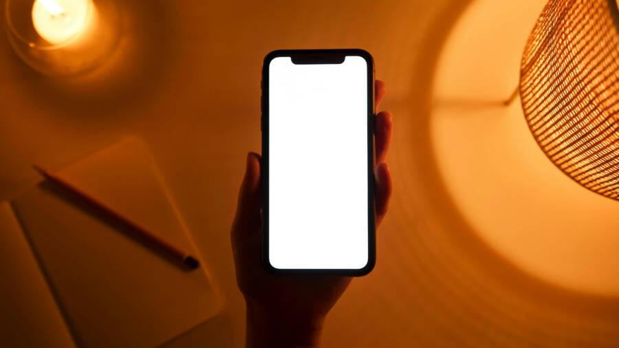 How to Set Different Wallpapers for Home and Lock Screens on Your Phone A hand holds a smartphone with a blank screen, illuminated by warm ambient light. Ideal for mockup designs.
