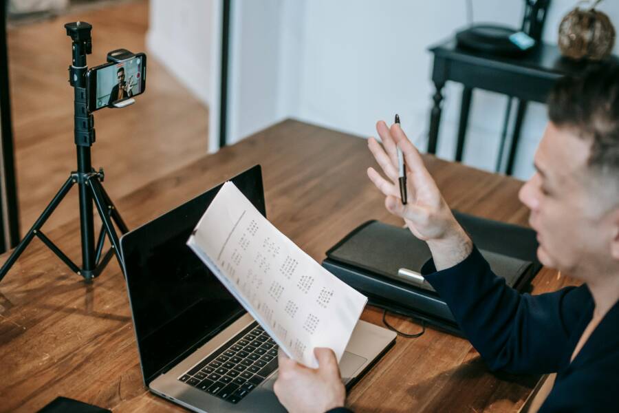 A man conducting an online teaching session using a laptop and smartphone on a tripod