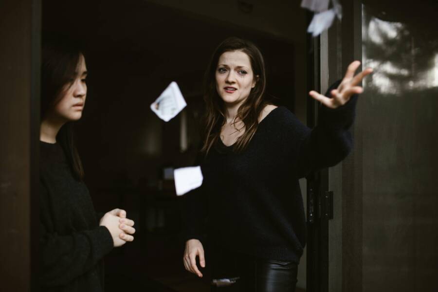 Two women in an emotional exchange, with one throwing papers dramatically indoors.