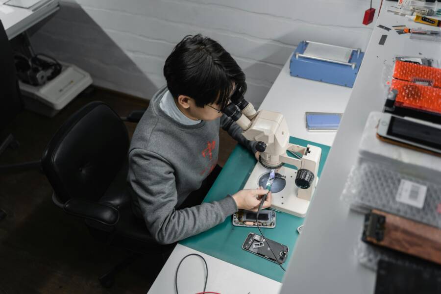 How to Fix Apps That Keep Crashing on Your Phone (Android & iPhone) Technician works on smartphone repair under a microscope, indoors at a tech bench.