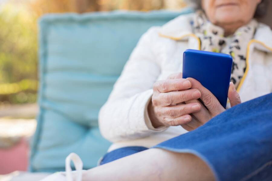 Senior woman holding a smartphone while relaxing outdoors, enjoying technology in a park setting.