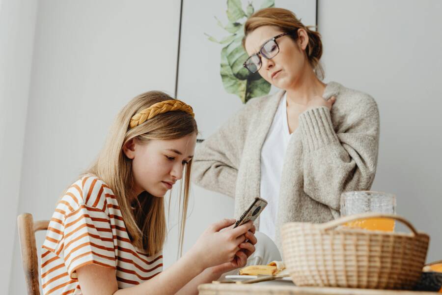 How to Make a Phone Safer for Kids (A Practical Guide) A mother discusses with her daughter engrossed in her phone during breakfast indoors