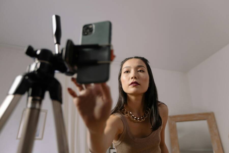 Asian woman setting up a smartphone on a tripod for vlogging indoors