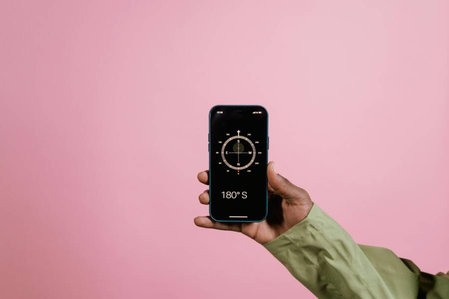 Close-up of a hand holding a smartphone displaying a compass app against a pink background