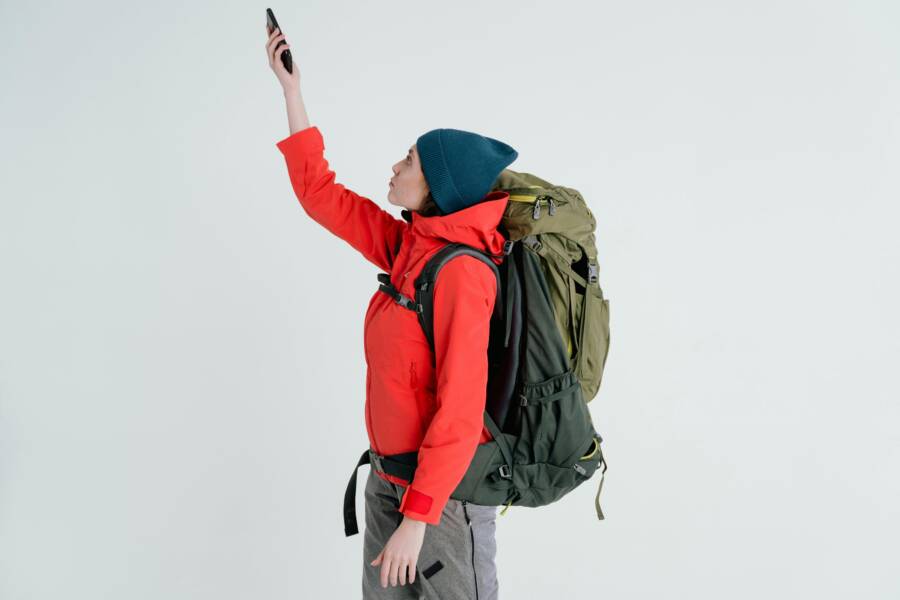 Outdoor explorer in winter clothes using cellphone to check signal while hiking with backpack.