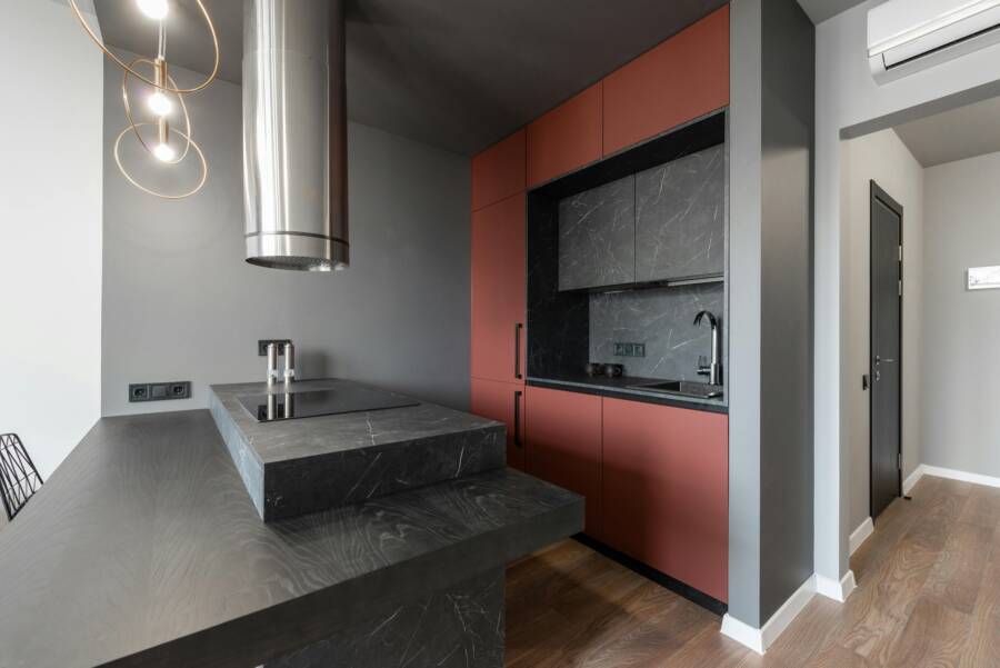 Contemporary minimalist island style kitchen with metal tube range hood over counter with built in stove in modern apartment