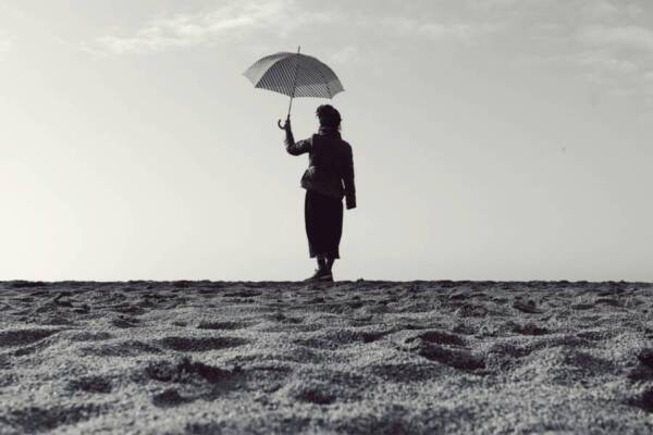 Black and white silhouette of a woman holding an umbrella while standing on a serene beach