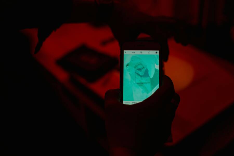 Close-up of hands using a smartphone camera in a low-light setting with red tones.