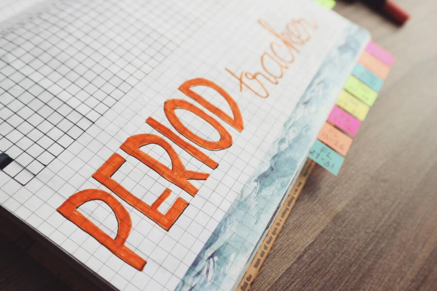 Close-up of a handwritten period tracker in a grid-lined journal on a wooden table