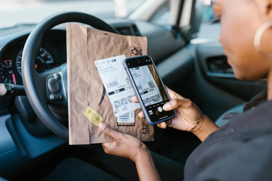 Close-up of a courier in a car scanning a package label with a smartphone for delivery service