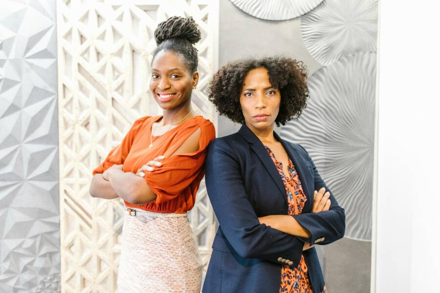 Two professional women with arms crossed in a modern office, exuding confidence and leadership.