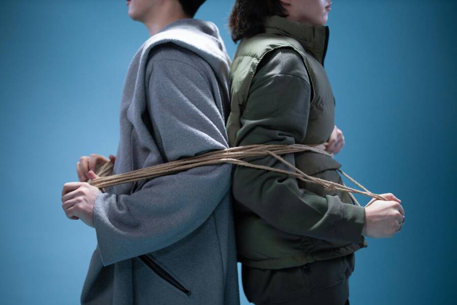 兩人背對背被繩綁，象徵連結與束縛