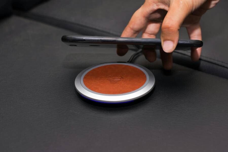 Close-up of a hand placing a smartphone on a wireless charging pad on a leather surface.