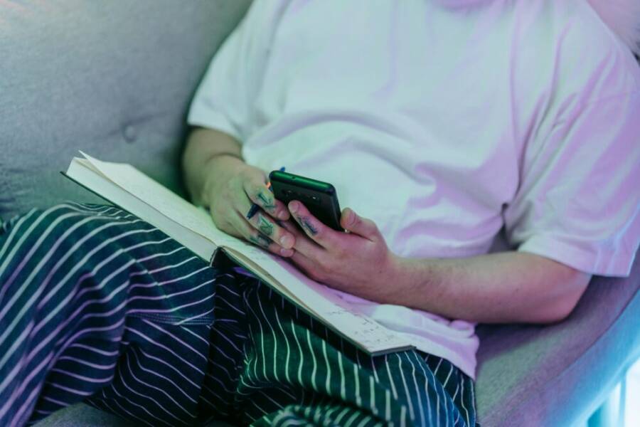 Seated individual holding a phone and pen, open notebook on lap
