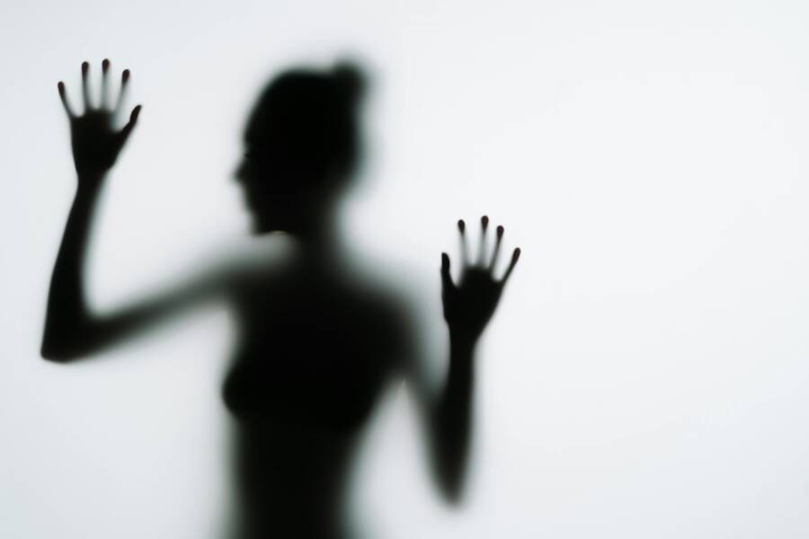Artistic silhouette of a woman pressing her hands against frosted glass, creating a mysterious effect.