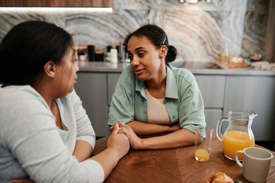 Two women engage in a supportive conversation over breakfast in a cozy kitchen setting