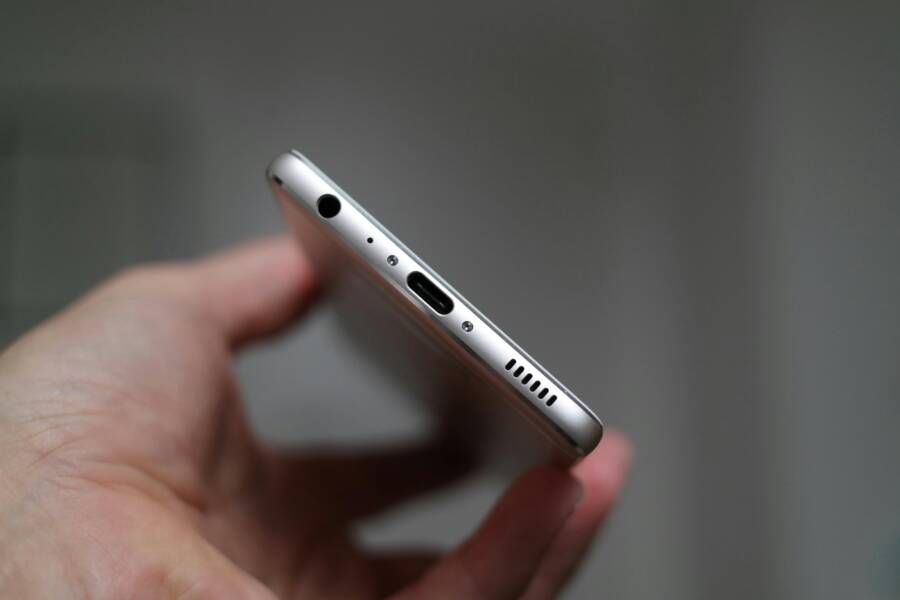 A close-up view of a person holding a smartphone, focusing on the charging port and headphone jack