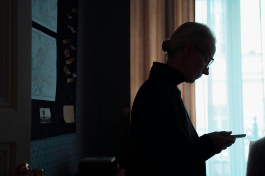 How to Make Text Bigger on Your Phone for Seniors (Easy Reading Tips) Silhouette of a senior woman looking at a smartphone in a dimly lit room, conveying introspection and solitude.