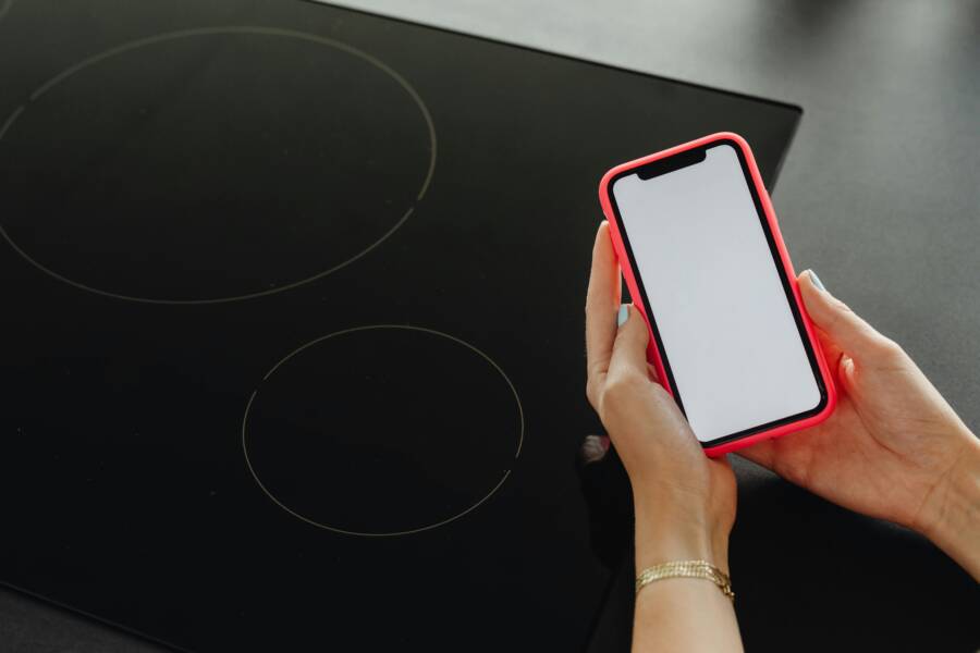 Close-up of hands holding a smartphone with a blank screen, beside a black cooktop