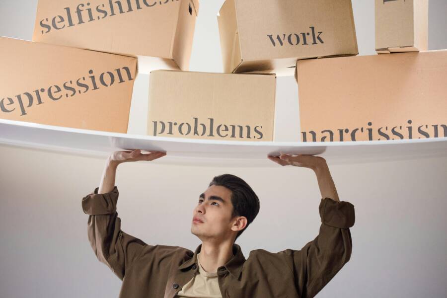 Young man struggles with metaphorical burdens symbolized by labeled boxes suspended above him.