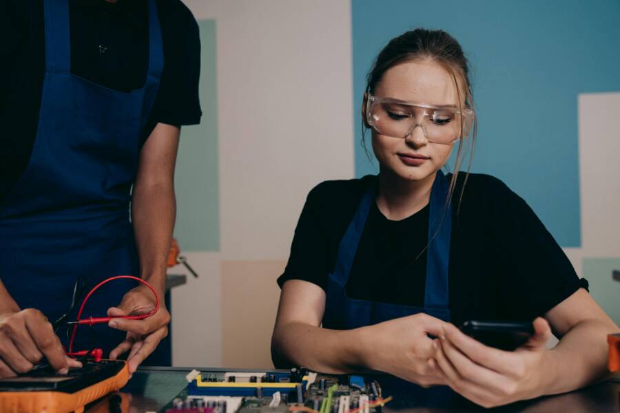 How to Fix Short Bluetooth Range on Your Smartphone (Pro Tips and Steps) Two young engineers working with electronics, using smartphones and safety glasses for protection.