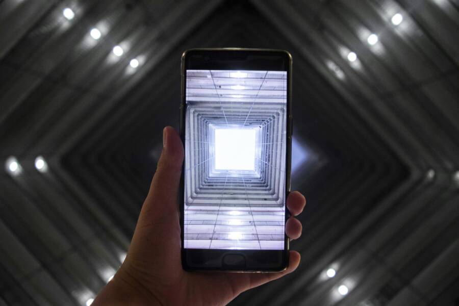 A smartphone screen captures a symmetrically illuminated building interior highlighting modern technology
