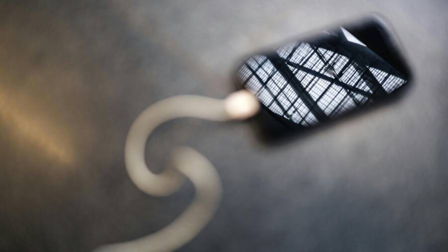 Smartphone showing architectural reflection, positioned with a white cable against a blurred background.