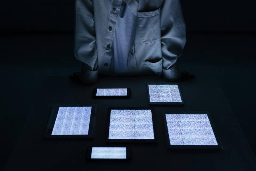 A person stands among multiple devices with screens on, a calm reminder to check real device issues first.